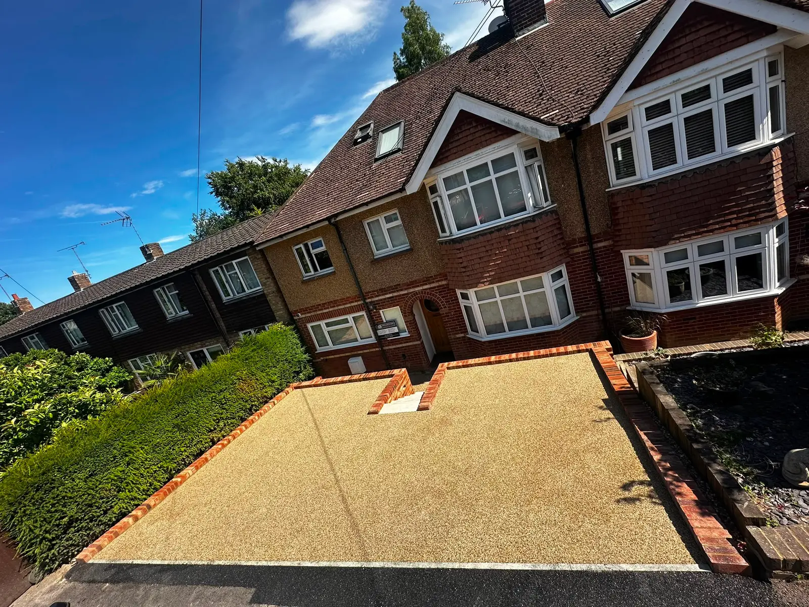 Buff resin bound driveway with brick edging in front of a semi-detached house